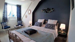Un dormitorio con una cama grande, dos mesitas de noche con lámparas, una silla, una pequeña mesa y una ventana con cortinas.