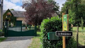 Una propiedad rural con una verja verde, un letrero que dice "La Bézardière" y un edificio cubierto de hiedra.