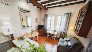 A cozy living room with a sofa, a dining table with chairs, a TV, and a large mirror. - Charming Getaway for Two: Historic Farm, Private Garden, Bikes & Ping-Pong Included (Souvigny-de-Touraine)