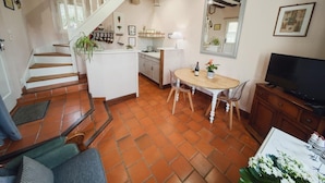 A spacious living area with a wooden staircase, a kitchen, a dining table, and a television. - Charming Getaway for Two: Historic Farm, Private Garden, Bikes & Ping-Pong Included (Souvigny-de-Touraine)