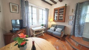 A cozy living room with a wooden table, a sofa, a TV, and a bookshelf. - Charming Getaway for Two: Historic Farm, Private Garden, Bikes & Ping-Pong Included (Souvigny-de-Touraine)