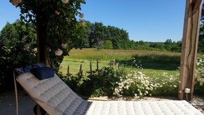 En enkel, vadderad loungestol med en mörk kudde, placerad under en träpergola med klätterrosor.