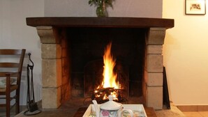 A fireplace with a burning fire, a wooden chair, and a table with a teapot and cups. - Semi-detached house with 4 bedrooms at Manoir de la Barguignerie (Saint-Christophe-du-Foc)