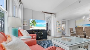 A spacious living room with a large TV, comfortable seating, and a view of the beach. - 2BR Condo Near Baytowne! Bay Views, Steps to Wharf, Pool/Hot Tub, Beach Tram. (Miramar Beach)