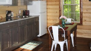 Une cuisine rustique aménagée dans une cabane en bois, avec un coin repas, un réfrigérateur blanc, un four à micro-ondes et un lustre.