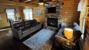 L’intérieur chaleureux d’un chalet en bois comprend une cheminée en pierre, des canapés en cuir et un coin repas.