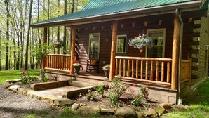 Une cabane rustique en rondins de bois, dotée d’une véranda, de balustrades en bois et de plantes en pot.