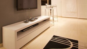 A modern living room with a flat-screen TV, a white entertainment unit, a black and white rug, and a unique ceiling light fixture. - Welcome Home (Sousse)