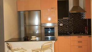 A compact kitchen with stainless steel appliances, a tiled backsplash, and two bar stools. - Welcome Home (Sousse)