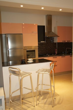 Una cocina moderna con electrodomésticos de acero inoxidable, un salpicadero de azulejos negros y dos taburetes de bar.