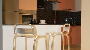 A modern kitchen with stainless steel appliances, a central island with bar stools, and a patterned backsplash. - Welcome Home (Sousse)