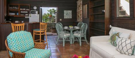 Un espacio de sala acogedor con muebles de mimbre, una mesa de centro de vidrio con flores y un sofá blanco con cojines decorativos.