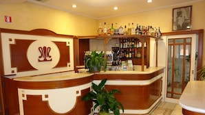 A bar area with a wooden counter, shelves of liquor bottles, and a potted plant. - Hotel Sollievo (San Giovanni Rotondo)