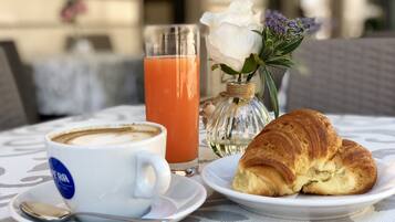 A table with a coffee cup, a glass of orange juice, a croissant, and a vase with flowers.