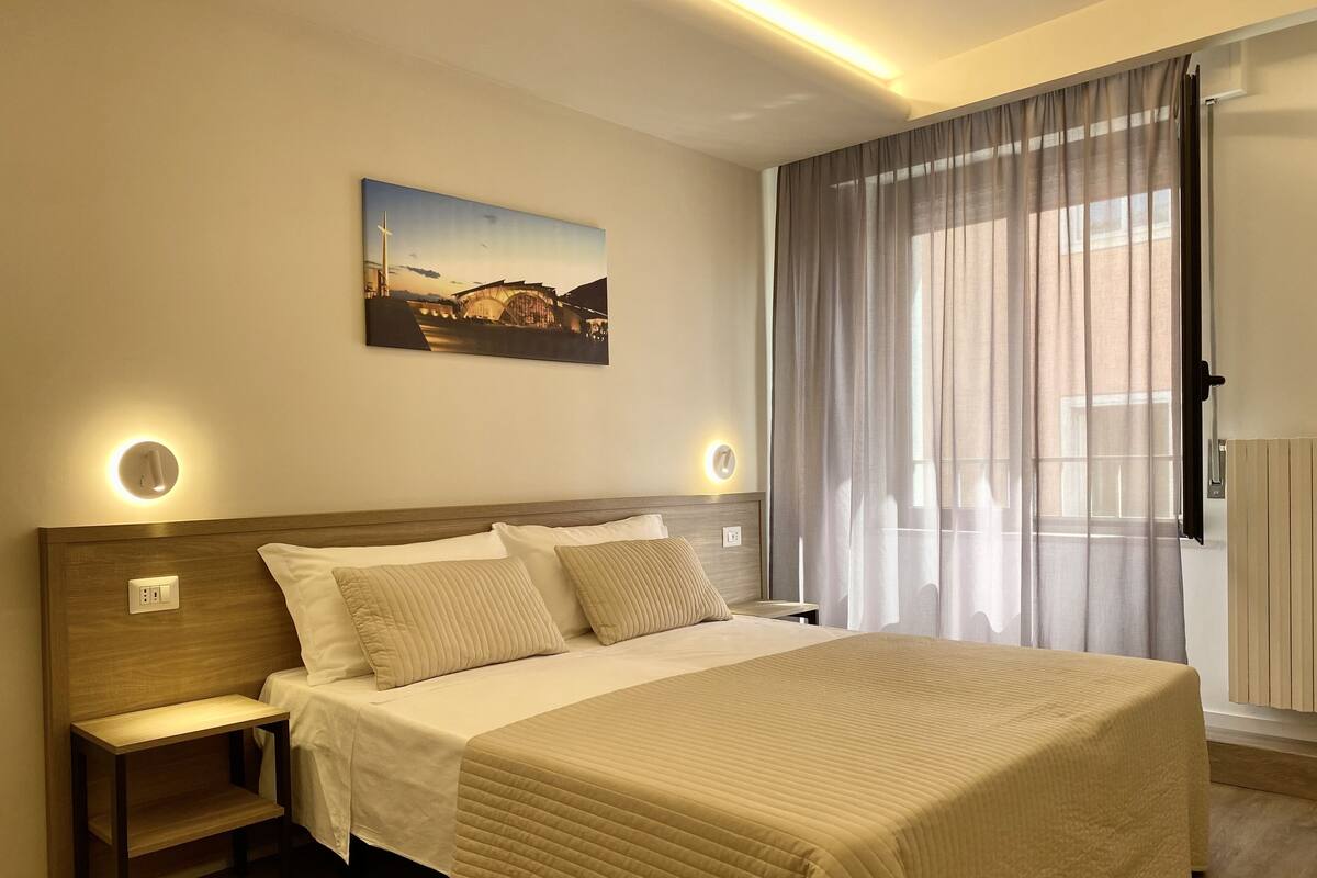 Une chambre d’hôtel avec un grand lit, des tables de chevet, un tableau au mur et une fenêtre avec des rideaux.