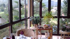 Un comedor con una mesa dispuesta para dos personas, una silla de mimbre y una mesita con una bandeja de condimentos.