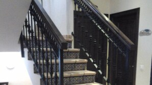 Una escalera con barandillas negras ornamentadas y peldaños beige con diseño.