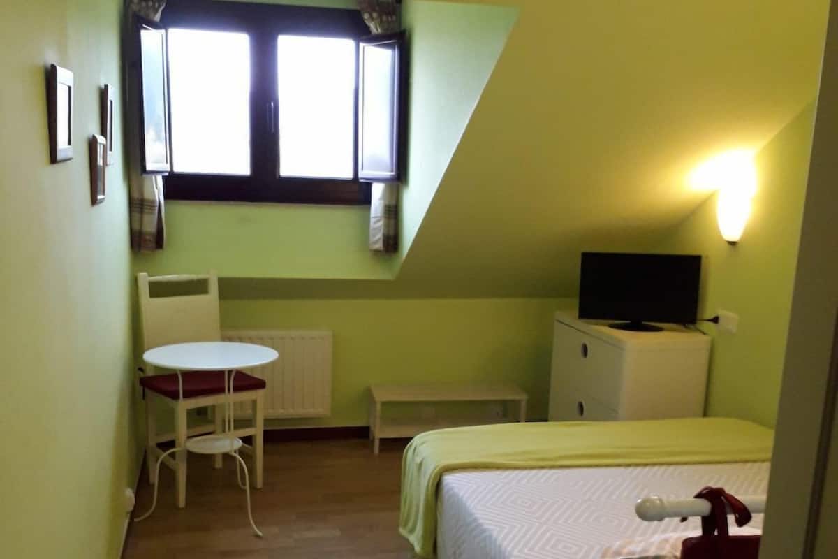 A small, single-room accommodation with a bed, a desk, and a television.