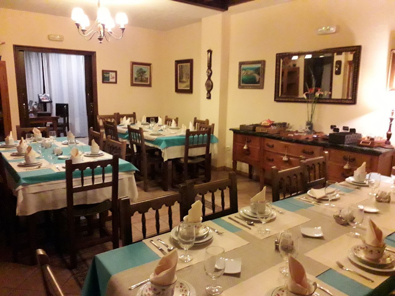 A dining area with multiple tables set for a meal, featuring wooden chairs and a chandelier.