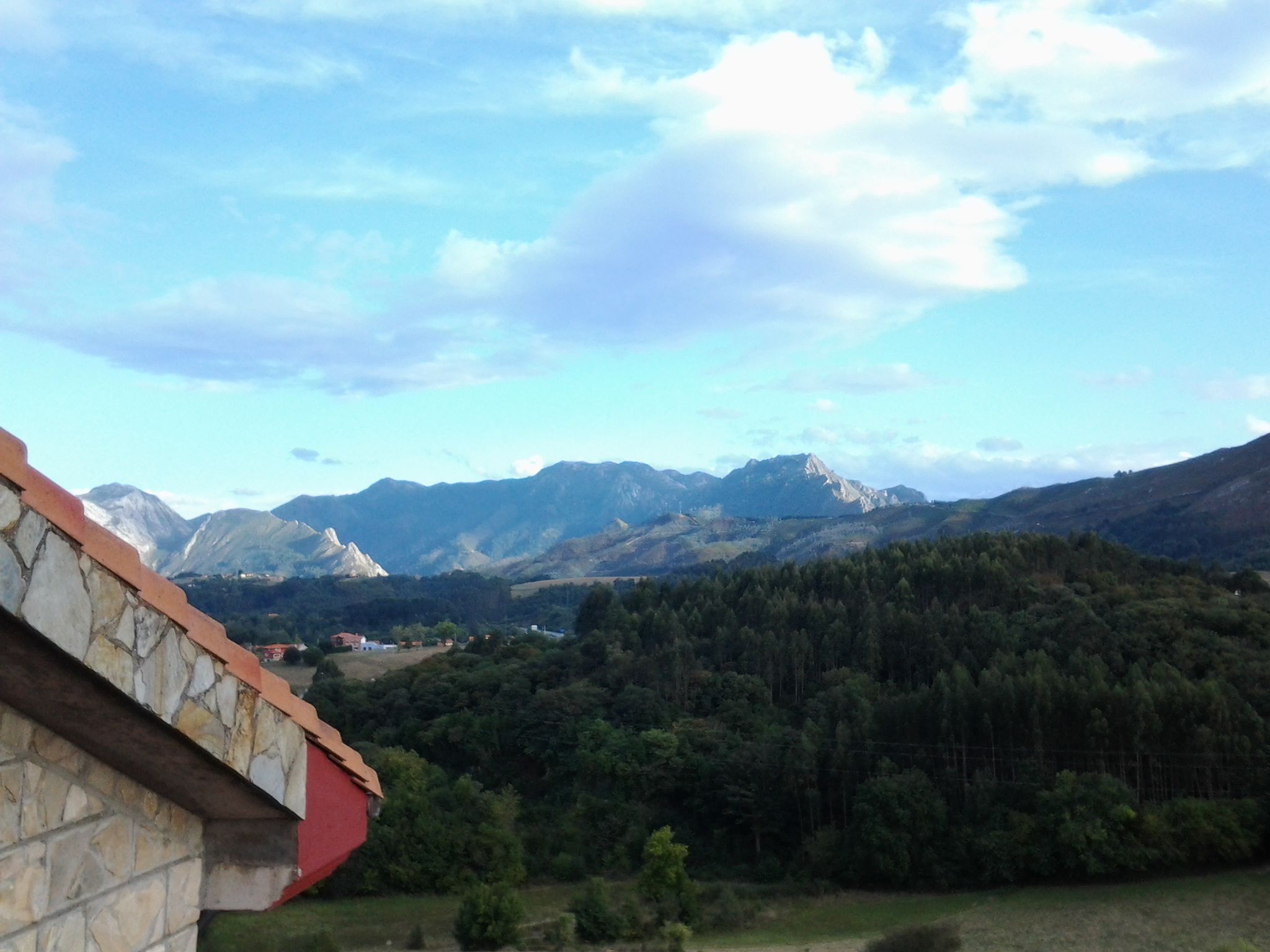 Paisatge de muntanyes amb un edifici de pedra i teulat vermell.