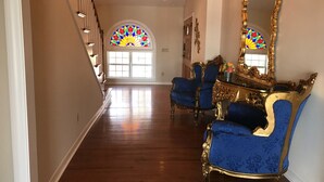 Un pasillo espacioso con piso de madera, una escalera con barandas blancas y un espejo grande y decorativo.