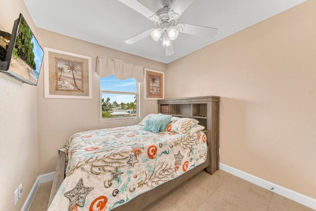 A bedroom with a bed, a ceiling fan, and two framed pictures on the wall.