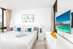 Quarto de hotel com uma cama, mesa de cabeceira, televisão e uma cesta de frutas.