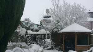 A gazebo covered in snow, a wooden bench, and a snow-covered tree in a garden. - Abels Appartements (Bochum)