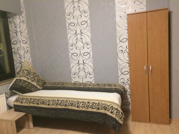 Une chambre à coucher avec un lit, deux oreillers, une armoire en bois et un papier peint à motifs.
