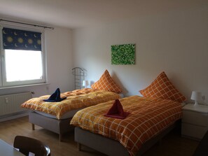 Une chambre avec deux lits, une fenêtre ornée d’un rideau représentant la lune et les étoiles, un tableau abstrait vert et un radiateur.