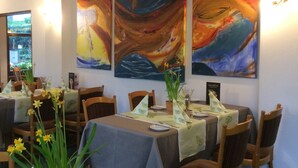 A dining area with tables set for two, featuring a large window with a view of greenery outside. - Abels Appartements (Bochum)