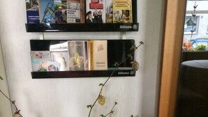 A shelf with books and a decorative arrangement including a teddy bear, flowers, and a small egg. - Abels Appartements (Bochum)