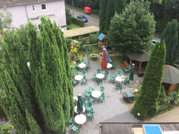 Un espacio de patio al aire libre con sillas y mesas de plástico verde, rodeado de árboles altos.