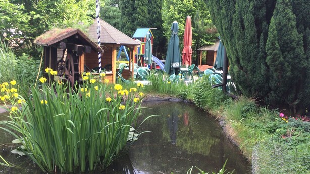 A garden with a pond, surrounded by greenery and a small wooden structure. - Abels Appartements (Bochum)