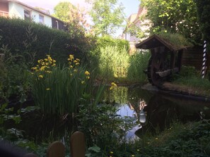 A garden with a pond, wooden structures, and dense foliage. - Abels Appartements (Bochum)