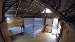 A room with a wooden ceiling, a bed with a mosquito net, a small table, and a window. - Safasurf Camp - Hostel (Arugam Bay)