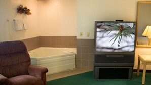 A room with a bathtub, a television displaying a nature scene, a brown armchair, and a small table with a lamp. - Odisha House of Rest (Shawano)