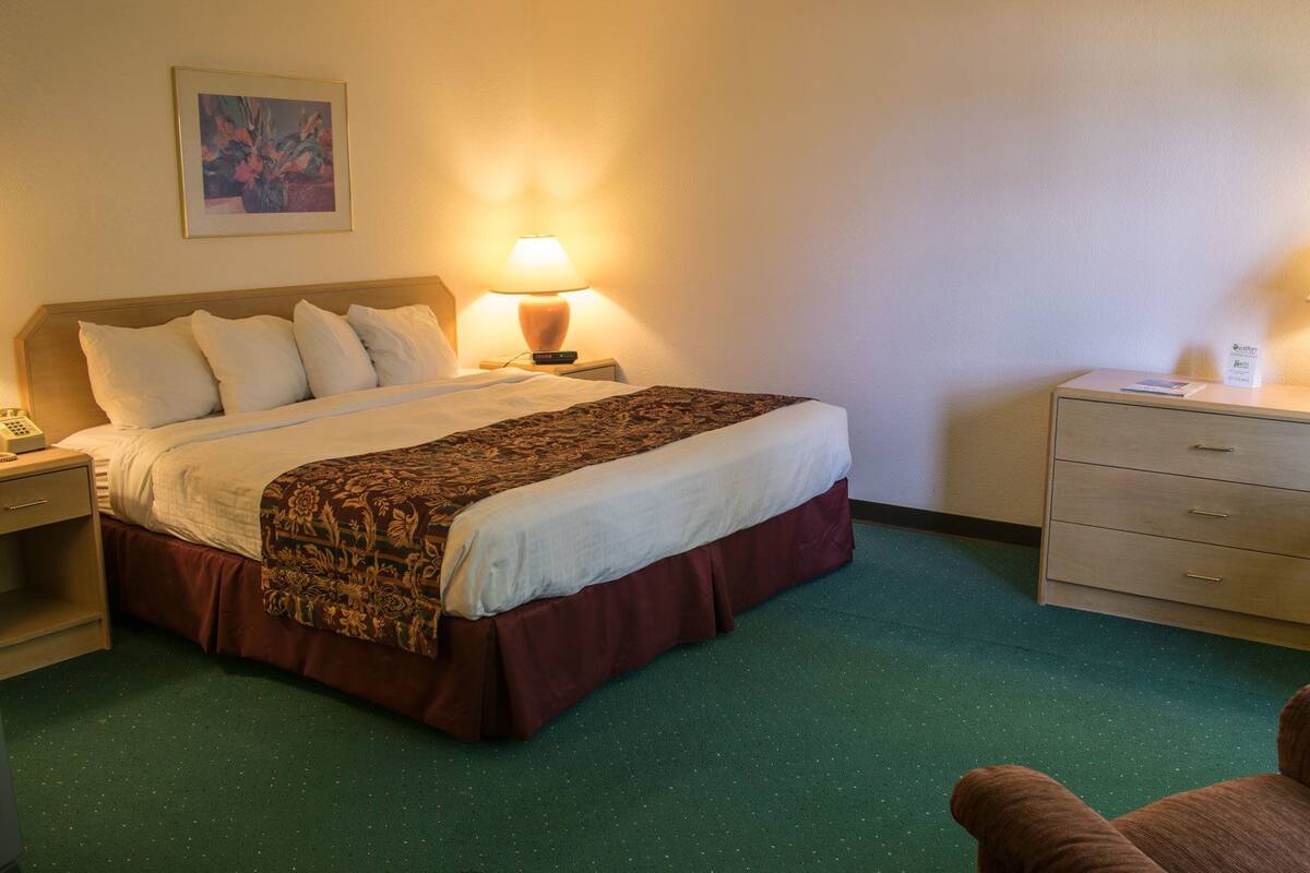 A hotel room with a bed, two bedside tables, a chair, and a desk with a lamp.