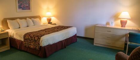 A hotel room with a bed, two bedside tables, a chair, and a desk with a lamp.