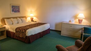 A hotel room with a bed, two bedside tables, a chair, and a desk with a lamp. - Odisha House of Rest (Shawano)