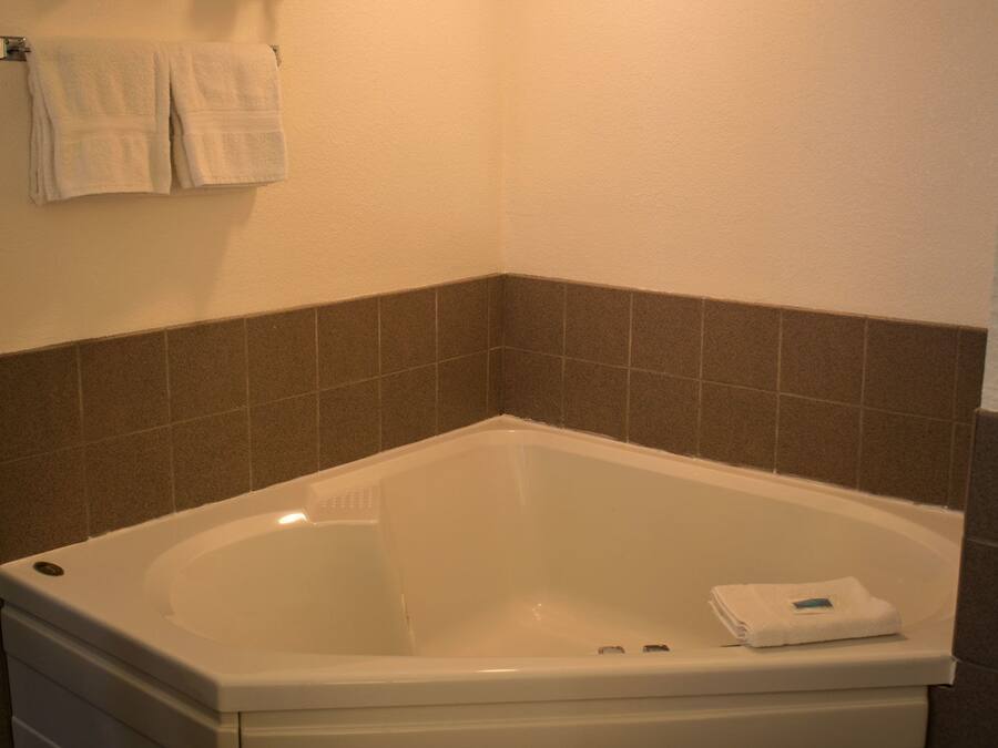 A bathroom with a white bathtub, a towel rack with two towels, and brown tiled walls.
