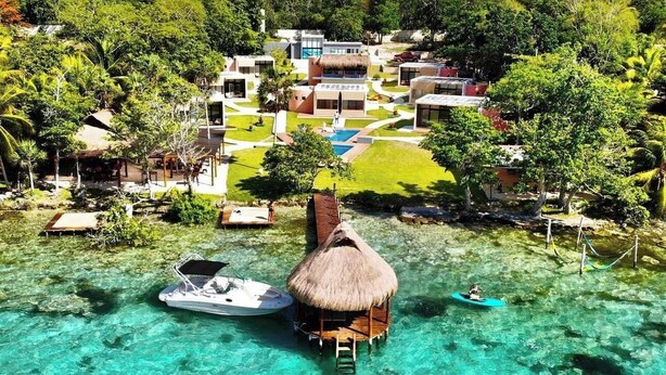 Un resort con bungalows sobre el agua, aguas turquesas cristalinas y exuberante vegetación.