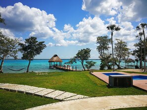 A beach view with a thatched-roof gazebo, a pool, and a grassy area with a concrete pathway.