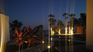 Vista nocturna de un complejo turístico con palmeras, una piscina y un sendero bien iluminado.