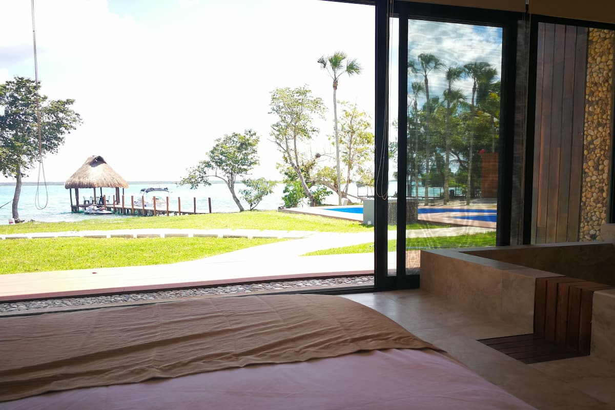 Una habitación con un ventanal grande que da a una piscina y una playa.