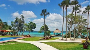 Zona de piscina en un resort, con vista despejada al océano, sillas de descanso y palmeras.