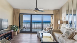 A spacious living room with a large television, comfortable seating, a ceiling fan, and a view of the ocean through a sliding glass door. - 314- BEACH FRONT, gulf view, family-friendly! Destin Beach Club (Destin)