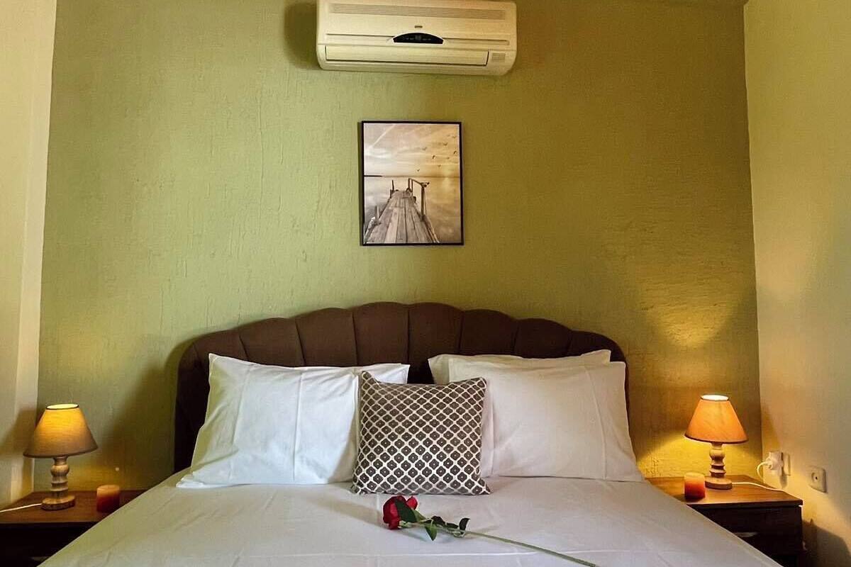 Una camera d'albergo con un letto, due lampade ai comodini, un condizionatore fissato al muro e un quadro incorniciato.