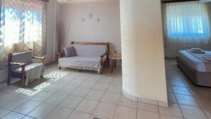 A spacious room with a high wooden ceiling, a bed, a sofa, and a small table. - Panorama beach (Chrani)