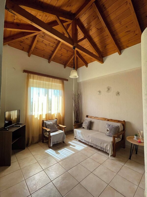 A cozy living room with a wooden ceiling, a sofa, a chair, a TV, and a small table with a plant. - Panorama beach (Chrani)